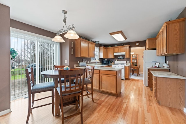 kitchen featuring under cabinet range hood, light countertops, white appliances, and a wealth of natural light