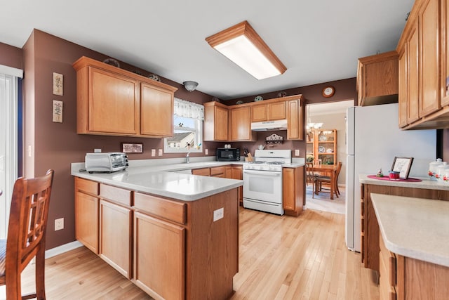 kitchen with a peninsula, under cabinet range hood, white appliances, and light countertops