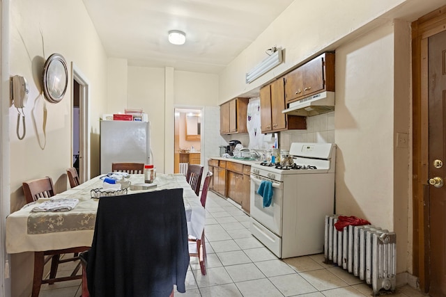 kitchen featuring white appliances, light countertops, radiator heating unit, under cabinet range hood, and brown cabinets