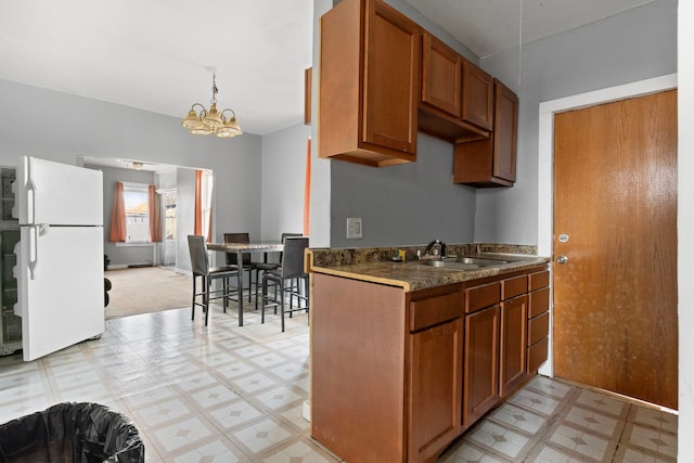 kitchen with a sink, freestanding refrigerator, light floors, and brown cabinets