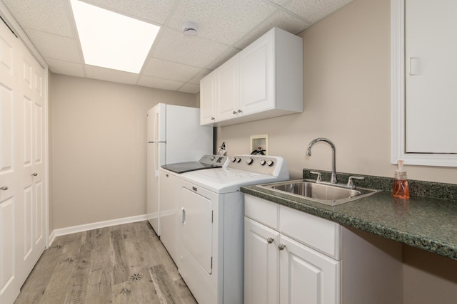 laundry room featuring independent washer and dryer, light wood-type flooring, cabinet space, a sink, and baseboards