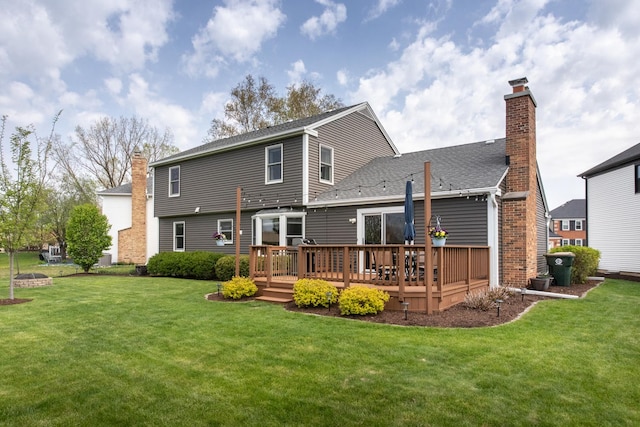 rear view of house with a lawn, a wooden deck, a shingled roof, and a chimney