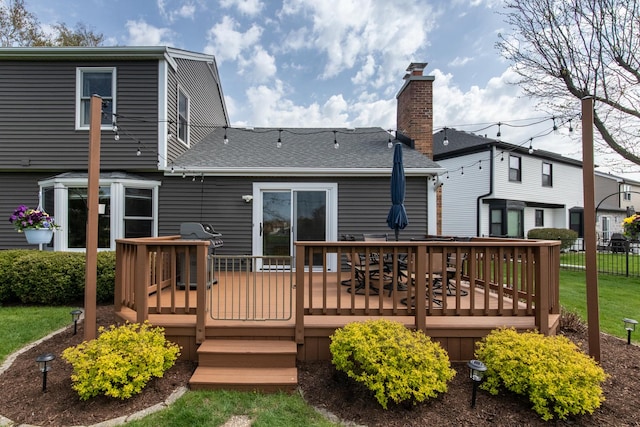 back of house with fence, a wooden deck, a chimney, a shingled roof, and a lawn