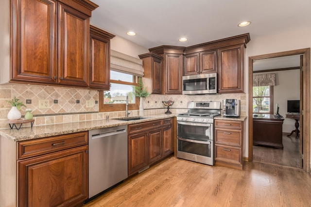 kitchen featuring decorative backsplash, appliances with stainless steel finishes, light stone countertops, a sink, and light wood finished floors
