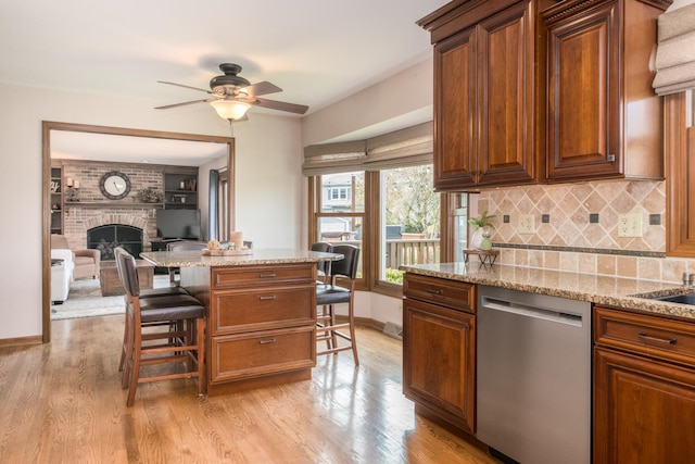 kitchen with light stone counters, a kitchen breakfast bar, a ceiling fan, light wood-type flooring, and stainless steel dishwasher
