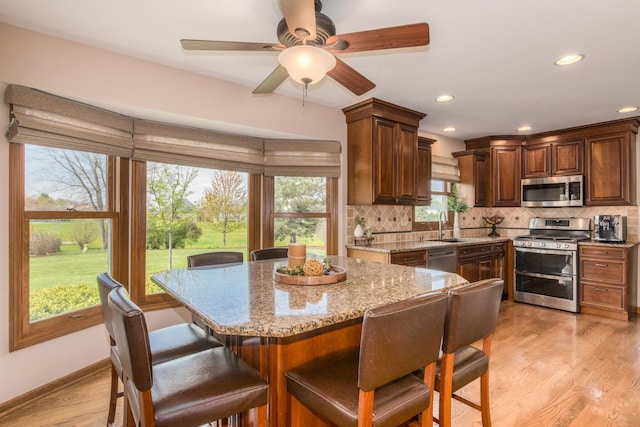 kitchen with a breakfast bar area, tasteful backsplash, light stone countertops, a sink, and stainless steel appliances