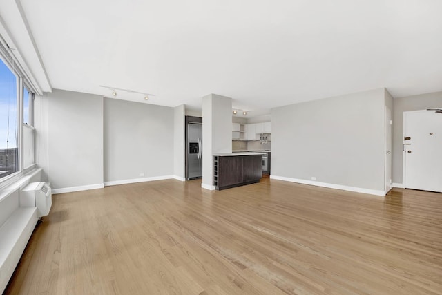 unfurnished living room with track lighting, baseboards, and light wood finished floors