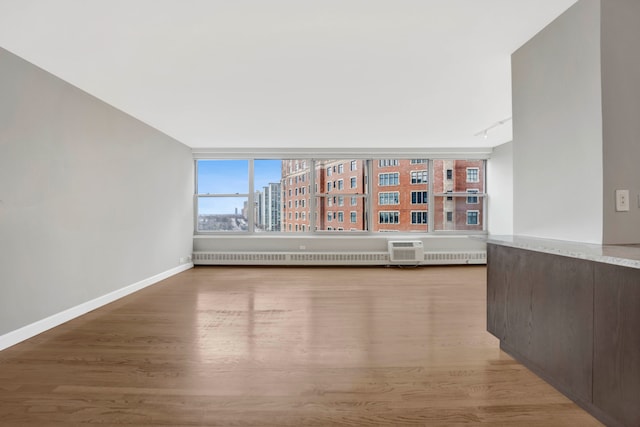 unfurnished living room featuring baseboards, light wood finished floors, radiator, and a view of city