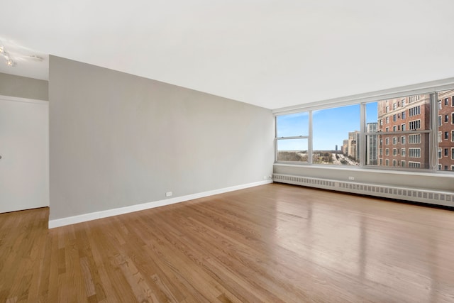 spare room with a baseboard radiator, wood finished floors, a view of city, and baseboards