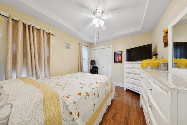bedroom featuring dark wood-style flooring, a tray ceiling, a ceiling fan, and a closet