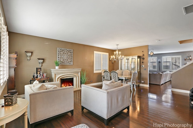 living area featuring a warm lit fireplace, a notable chandelier, dark wood finished floors, and visible vents