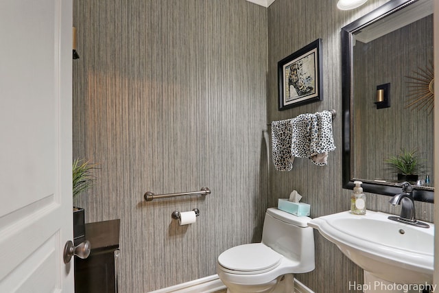 bathroom featuring toilet, wallpapered walls, and a sink