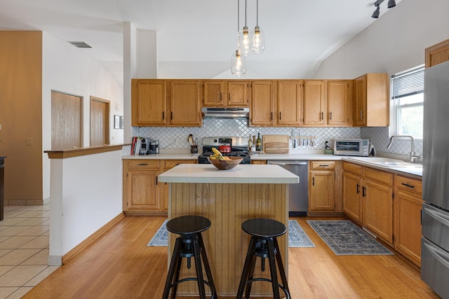 kitchen featuring stainless steel appliances, under cabinet range hood, a sink, light countertops, and vaulted ceiling
