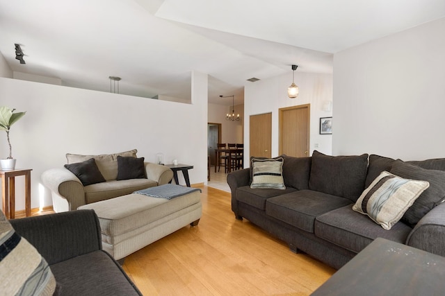 living room featuring a chandelier, light wood-type flooring, and lofted ceiling