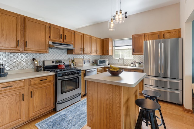 kitchen featuring appliances with stainless steel finishes, under cabinet range hood, a sink, light countertops, and tasteful backsplash