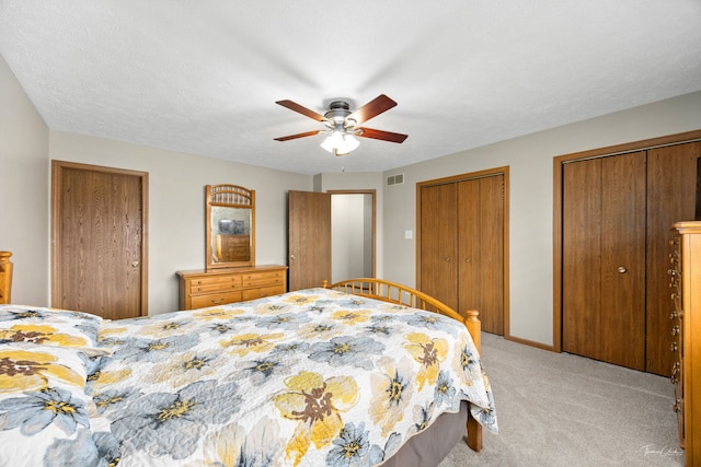 bedroom with two closets, visible vents, a ceiling fan, and light colored carpet