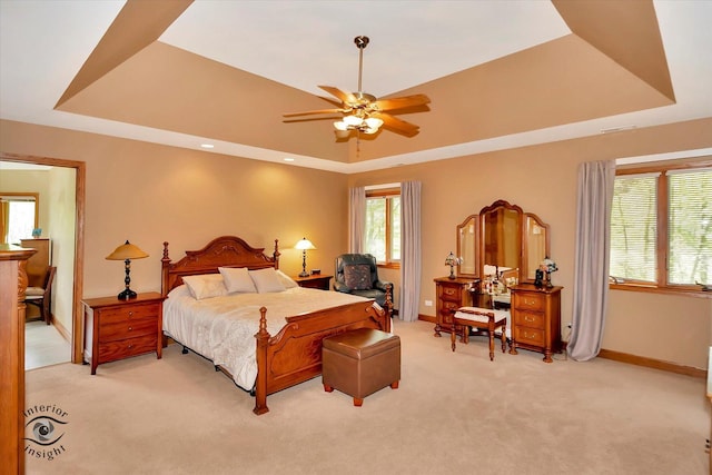 bedroom with a raised ceiling, light carpet, baseboards, and a ceiling fan