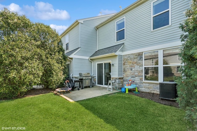 rear view of house with central AC unit, stone siding, a patio, a lawn, and a shingled roof