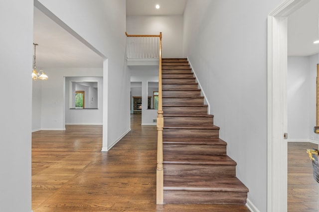 stairway with wood finished floors, a notable chandelier, baseboards, a towering ceiling, and recessed lighting