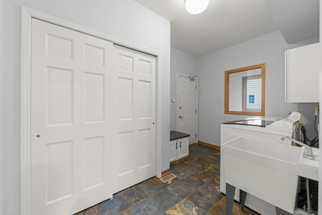 laundry room featuring baseboards, cabinet space, a sink, and stone tile flooring