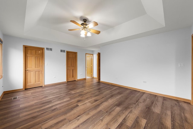 unfurnished bedroom with a tray ceiling, baseboards, dark wood-style floors, and visible vents