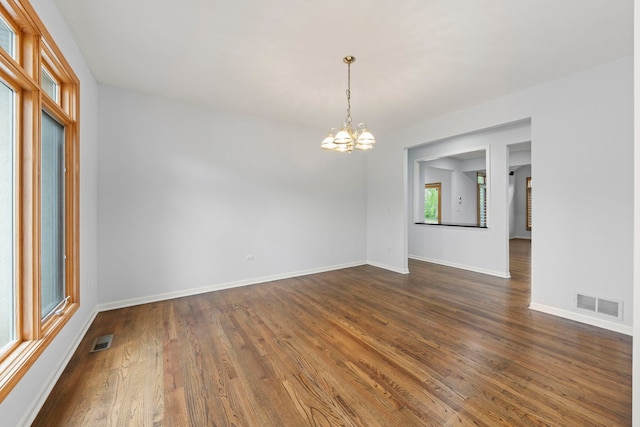 empty room with baseboards, dark wood-style flooring, a notable chandelier, and visible vents