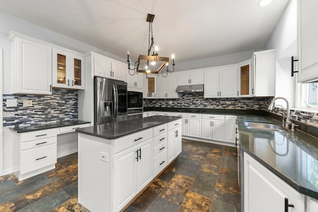 kitchen with a sink, tasteful backsplash, black appliances, under cabinet range hood, and stone tile floors