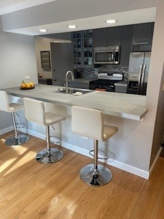 kitchen with wood finished floors, dark cabinetry, a sink, a kitchen bar, and appliances with stainless steel finishes