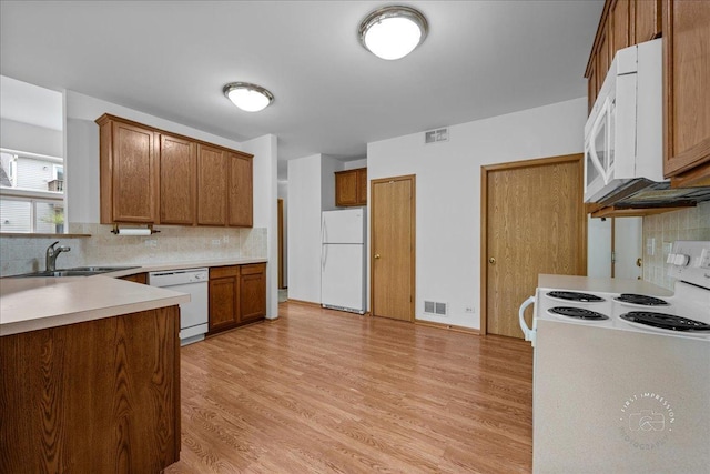 kitchen featuring white appliances, brown cabinetry, decorative backsplash, and a sink