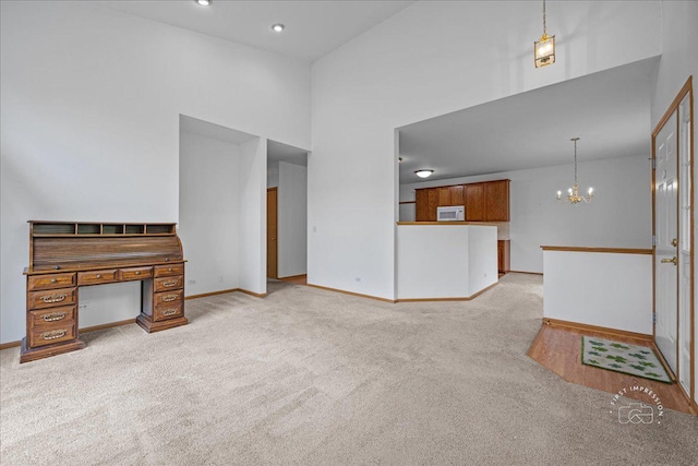 unfurnished living room with light carpet, a chandelier, baseboards, and a high ceiling