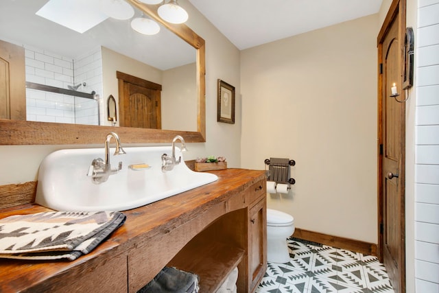 bathroom featuring a tile shower, tile patterned flooring, toilet, vanity, and a skylight