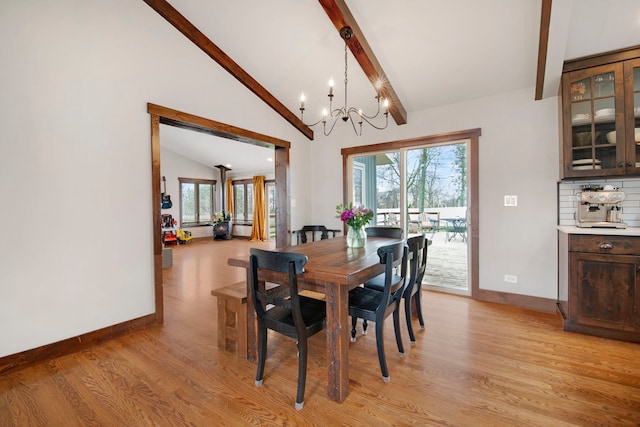 dining room featuring light wood-style flooring, a wealth of natural light, vaulted ceiling with beams, baseboards, and an inviting chandelier