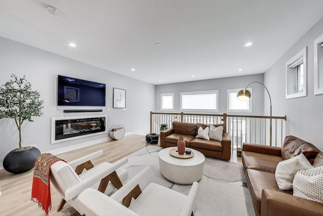 living room featuring light wood-style flooring, recessed lighting, a glass covered fireplace, and baseboards