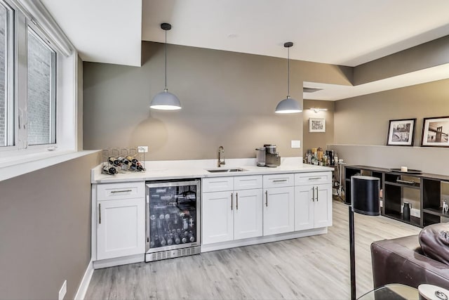 bar featuring wet bar, a sink, decorative light fixtures, wine cooler, and light wood finished floors
