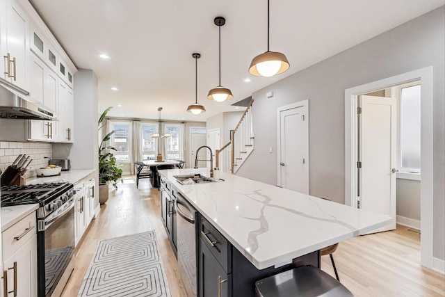 kitchen featuring stainless steel range with gas stovetop, light wood-style flooring, white cabinetry, a sink, and a center island with sink