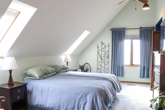 carpeted bedroom featuring vaulted ceiling with skylight, baseboards, a ceiling fan, and visible vents