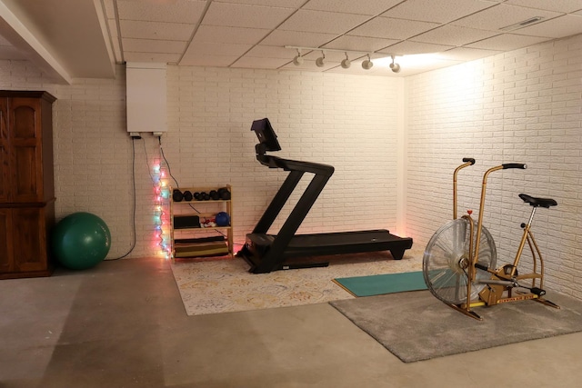 workout room with brick wall, a drop ceiling, and rail lighting