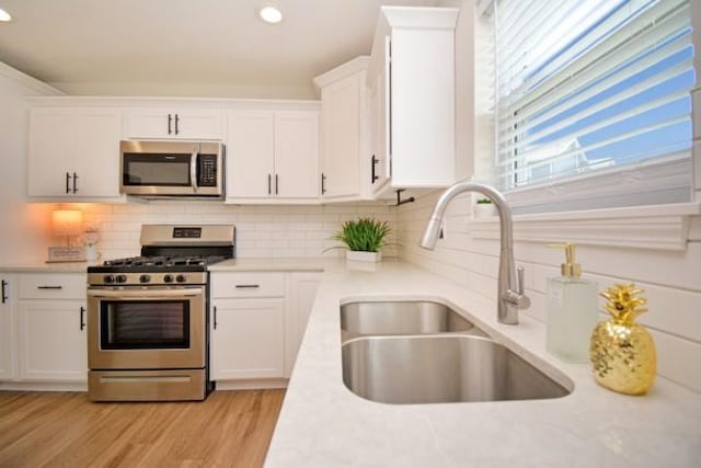 kitchen featuring white cabinets, stainless steel appliances, light countertops, and a sink