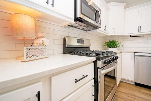 kitchen with light countertops, light wood-type flooring, decorative backsplash, appliances with stainless steel finishes, and white cabinetry