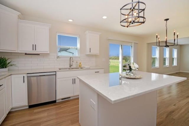 kitchen featuring backsplash, dishwasher, a sink, light wood-style floors, and a chandelier