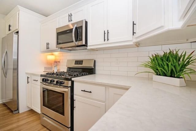 kitchen with backsplash, appliances with stainless steel finishes, light wood finished floors, and white cabinetry