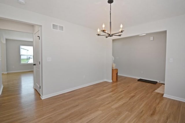 unfurnished dining area featuring baseboards, wood finished floors, visible vents, and a notable chandelier