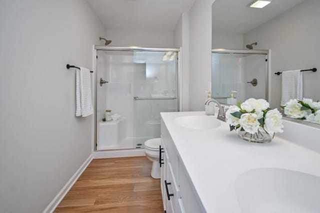 bathroom with a shower stall, wood finished floors, a sink, double vanity, and toilet