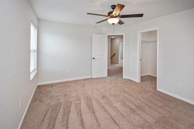 unfurnished bedroom with carpet, a spacious closet, a closet, baseboards, and ceiling fan