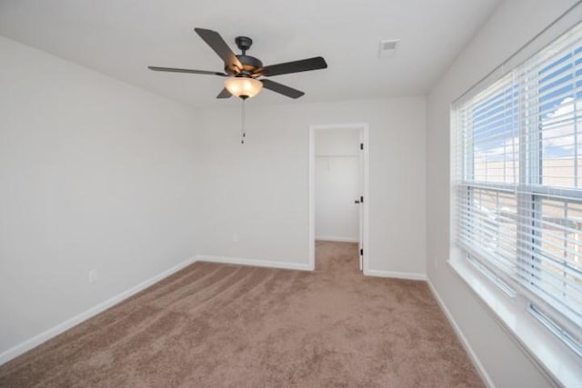 carpeted spare room with visible vents, a ceiling fan, and baseboards
