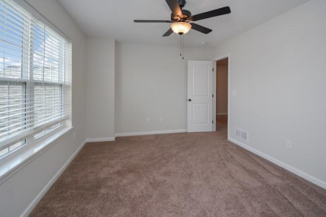 carpeted empty room with a ceiling fan, baseboards, a healthy amount of sunlight, and visible vents