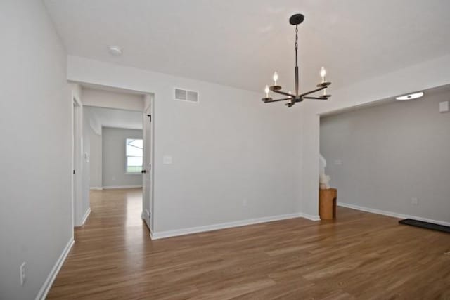 spare room featuring an inviting chandelier, wood finished floors, visible vents, and baseboards