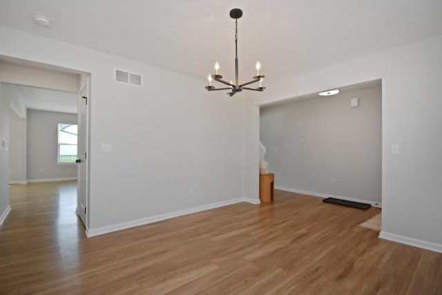 empty room with wood finished floors, visible vents, baseboards, and an inviting chandelier