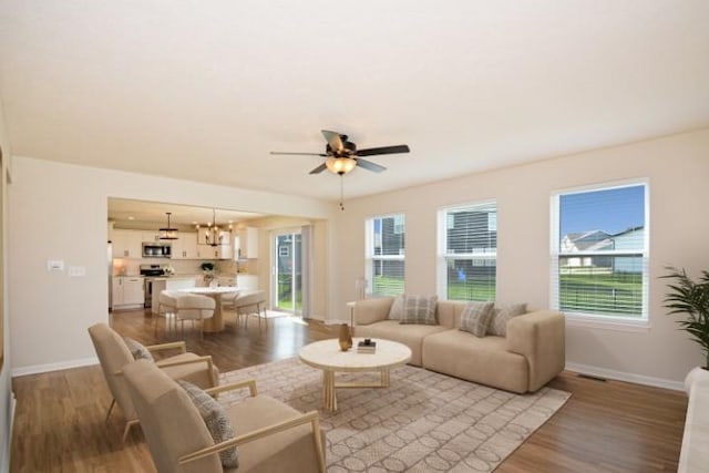 living room with light wood finished floors, baseboards, visible vents, and ceiling fan with notable chandelier