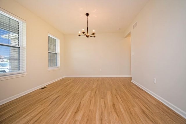 unfurnished room featuring an inviting chandelier, visible vents, light wood finished floors, and baseboards